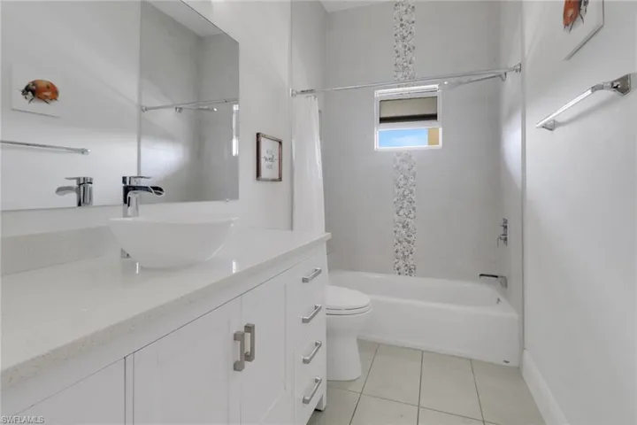 Bathroom with toilet, shower / bath combo with shower curtain, vanity, and tile patterned floors