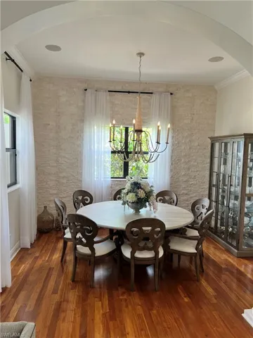 Dining area with arched walkways, crown molding, a chandelier, and wood finished floors