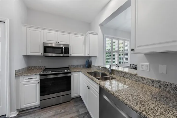 Kitchen featuring white cabinetry, light stone counters, stainless steel appliances, and sink