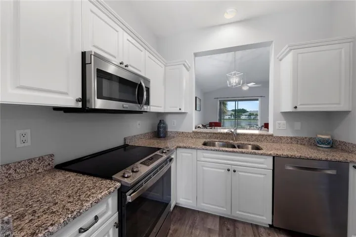 Kitchen with vaulted ceiling, stainless steel appliances, dark hardwood / wood-style flooring, white cabinetry, and sink