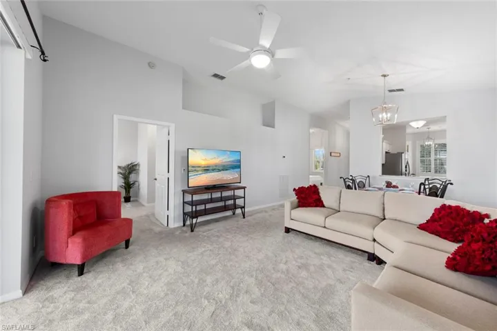 Living room with vaulted ceiling, ceiling fan with notable chandelier, and light carpet