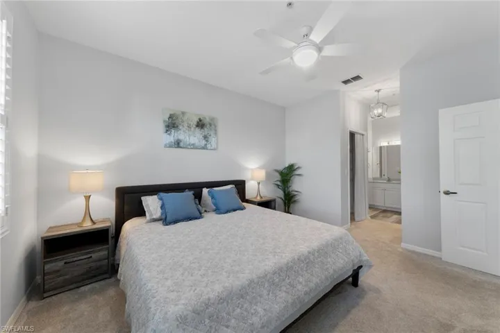 Bedroom featuring ceiling fan, sink, light carpet, and ensuite bath