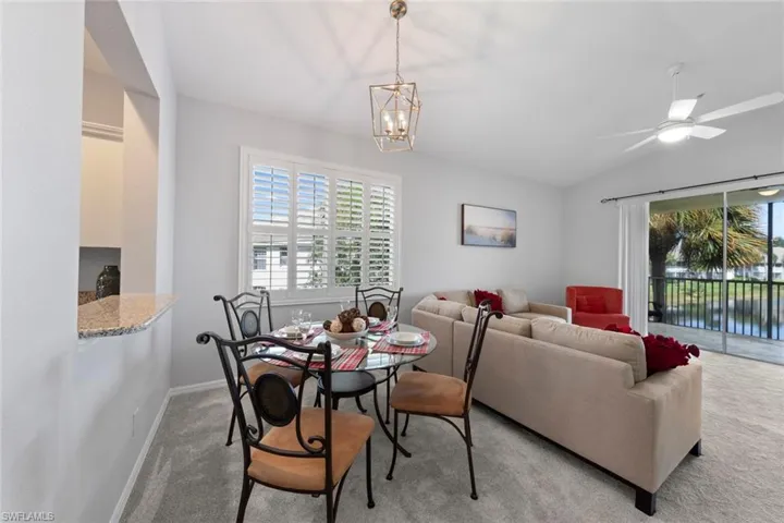 Carpeted dining room with ceiling fan with notable chandelier and lofted ceiling