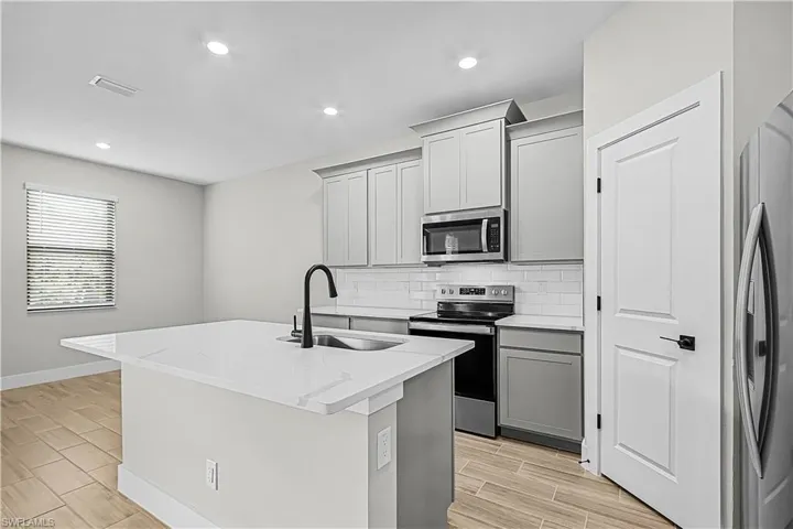 Kitchen featuring appliances with stainless steel finishes, wood tiled floors, gray cabinetry, backsplash, and a center island with sink