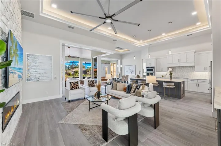 Living room featuring ceiling fan, light plank ceramic tile flooring, a fireplace, and a tray ceiling