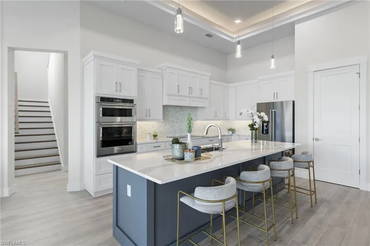 Kitchen featuring hanging light fixtures, an island with sink, a kitchen bar, white cabinetry, and stainless steel appliances