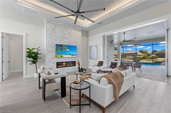 Living room featuring ceiling fan, a fireplace, a tray ceiling