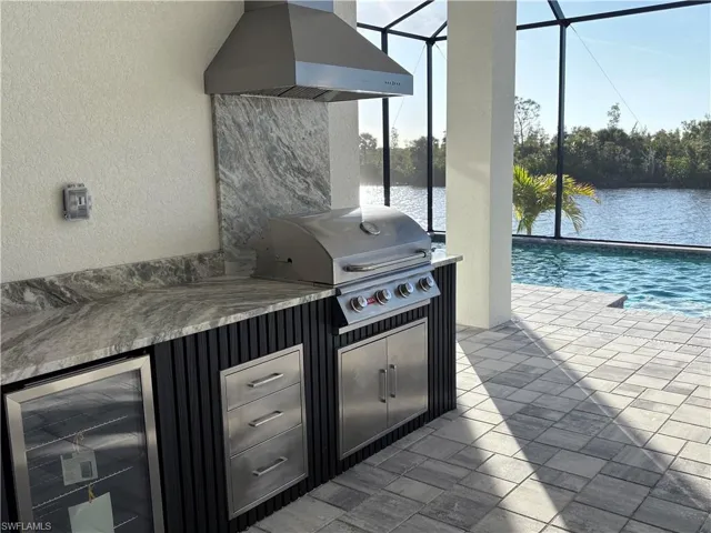 View of patio / terrace with area for grilling, exterior bar, beverage cooler, a water view, and glass enclosure