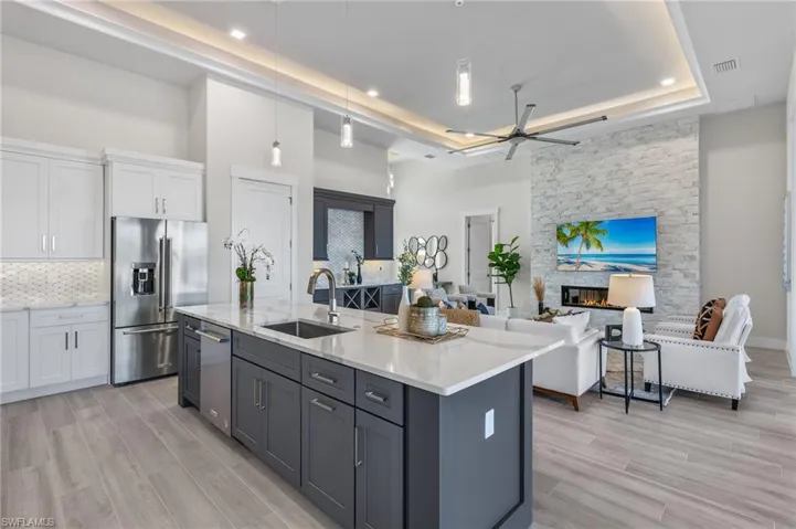 Kitchen with white cabinetry, sink, hanging light fixtures, high end refrigerator, and a center island with sink