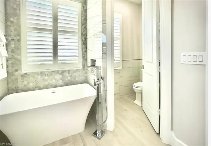 Bathroom featuring a bathing tub, wood-type flooring, tile walls, and toilet