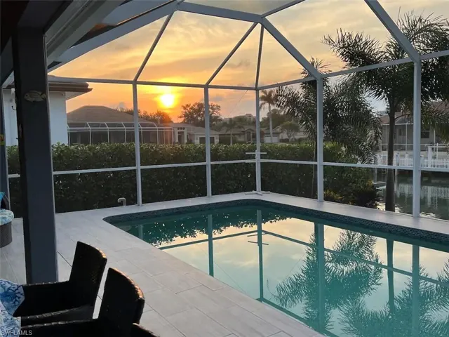 Pool at dusk featuring glass enclosure and a patio