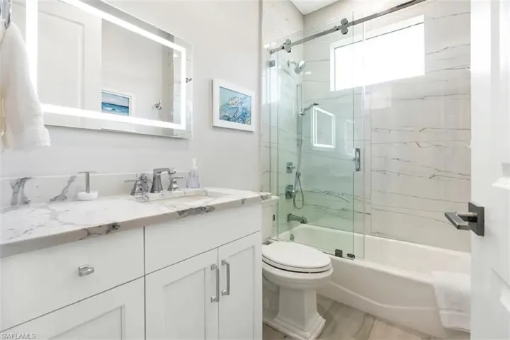 Full bathroom with enclosed tub / shower combo, vanity, and toilet