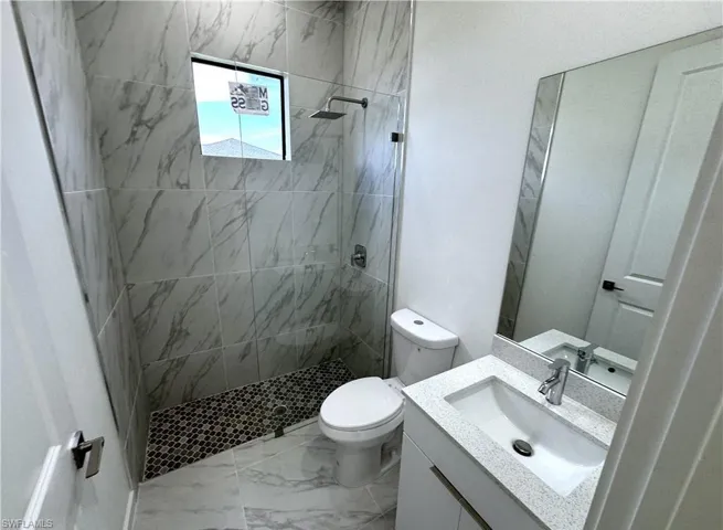 Full bathroom featuring vanity, tiled shower, and light marble finish flooring