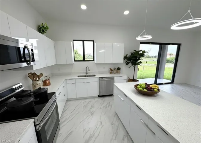 Kitchen featuring stainless steel appliances, modern cabinets, white cabinetry, light marble finish floors, and hanging light fixtures