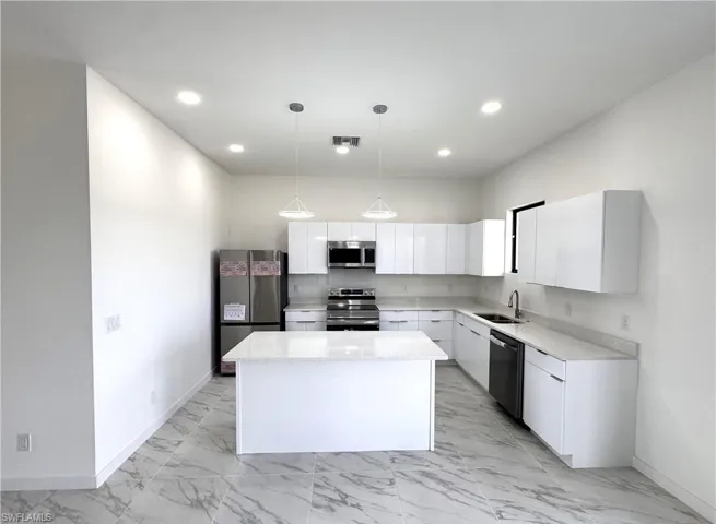 Kitchen with stainless steel appliances, white cabinetry, light stone countertops, and a center island