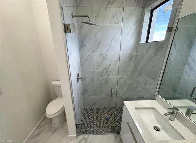 Bathroom with vanity, a marble finish shower, and light marble finish flooring