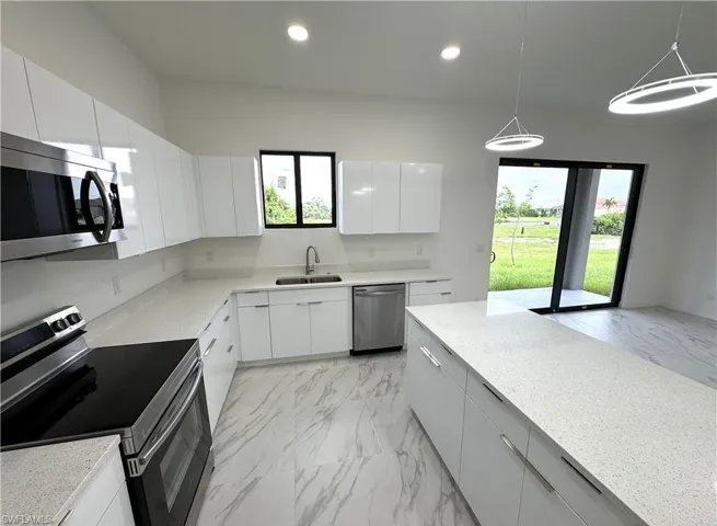 Kitchen with stainless steel appliances, light marble finish floors, modern cabinets, hanging light fixtures, and white cabinetry