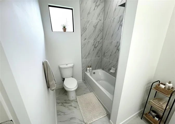 Full bath with light marble finish flooring and shower / bathtub combination