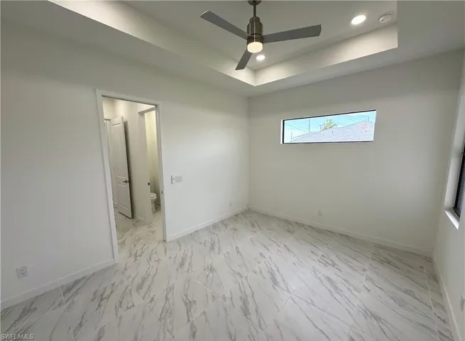 Unfurnished bedroom with recessed lighting, light marble finish flooring, ceiling fan, and a raised ceiling