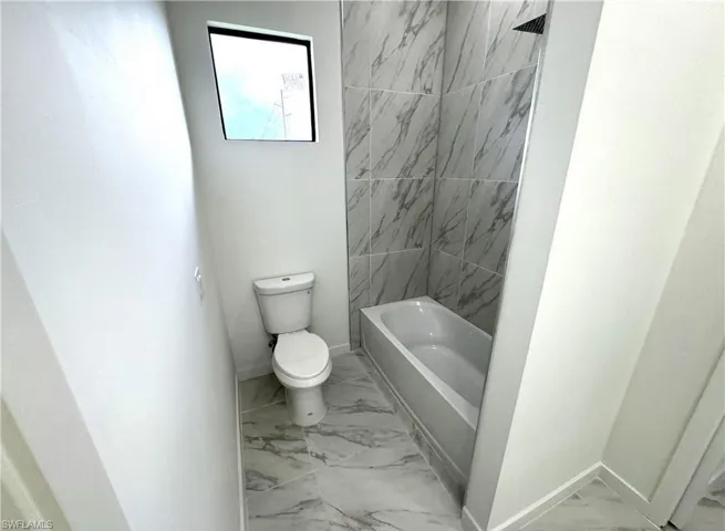Full bath with light marble finish floors and  shower combination