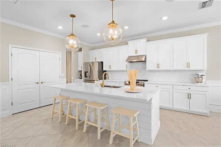 Kitchen with a center island with sink, pendant lighting, appliances with stainless steel finishes, sink, and white cabinets