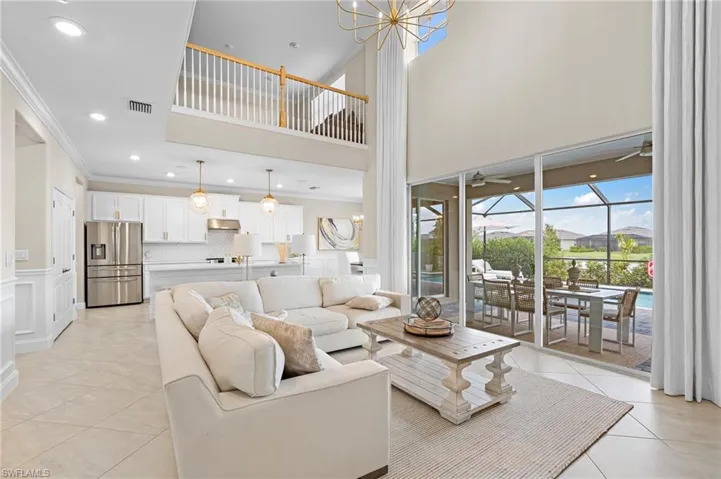Living room with light tile patterned floors, a high ceiling, ornamental molding, and ceiling fan with notable chandelier
