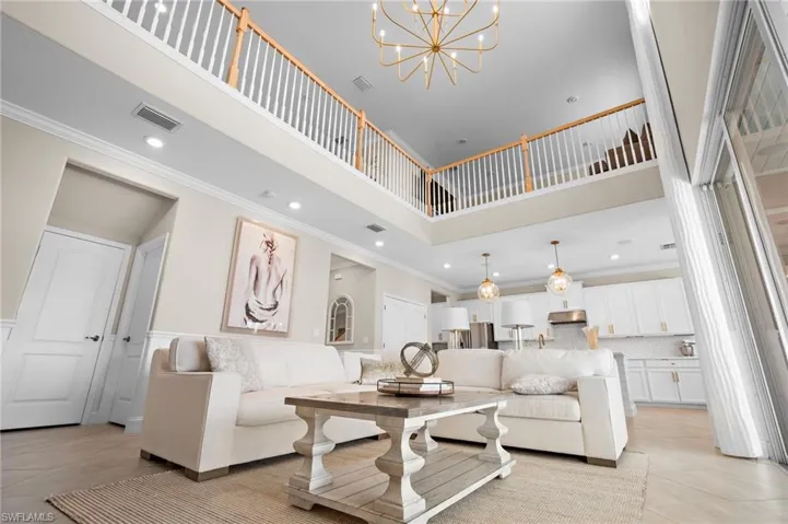Living room with a high ceiling, an inviting chandelier, light tile patterned flooring, and ornamental molding