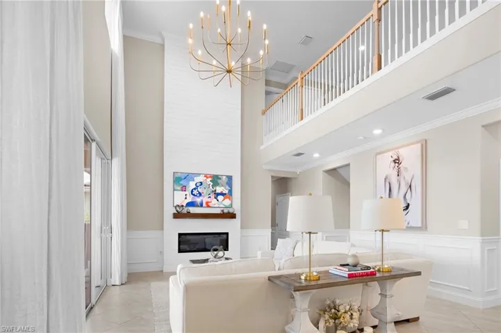 Tiled living room with a large fireplace, a high ceiling, ornamental molding, and a chandelier