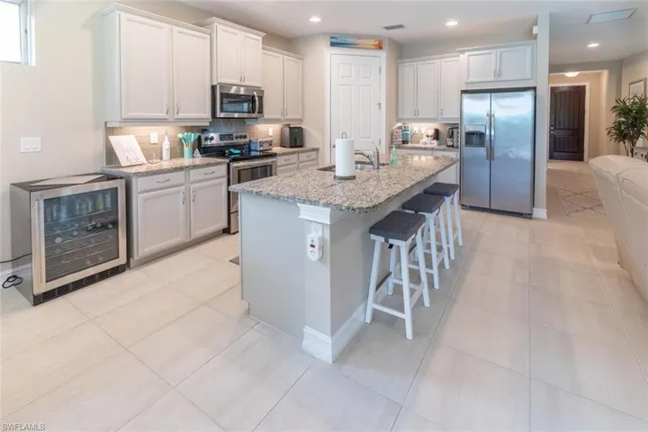 Kitchen featuring stainless steel appliances, white cabinetry, light tile flooring, and beverage cooler