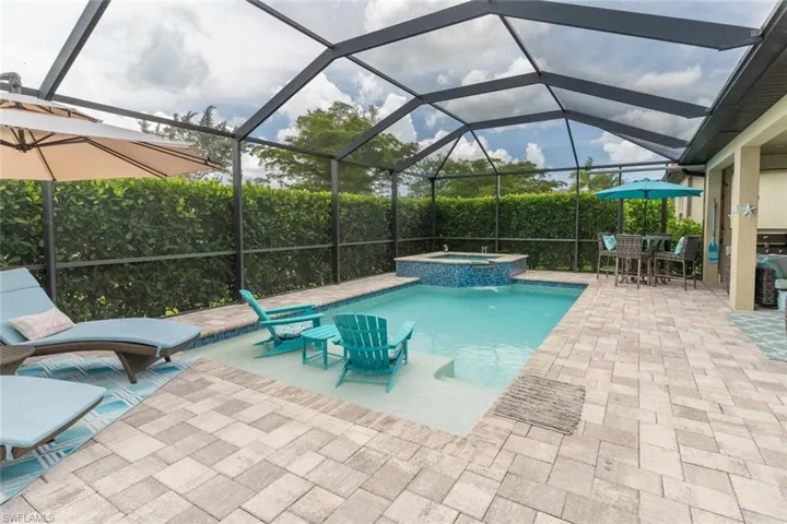 View of swimming pool with an in ground hot tub, glass enclosure, and a patio area