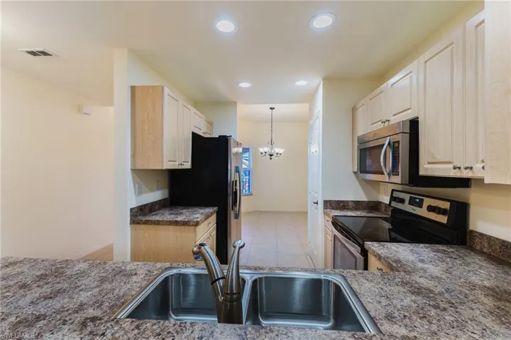 Kitchen with stainless steel appliances, light wood finish cabinetry, suspended lighting, light tile patterned floors, and dark stone counters