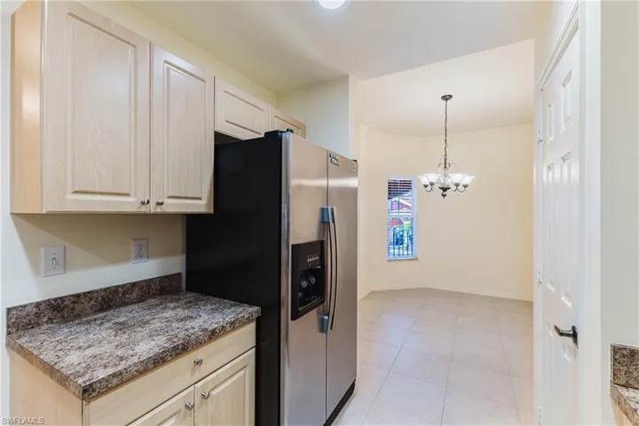 Kitchen featuring dark countertops, suspended lighting, stainless steel refrigerator with ice dispenser, light tile patterned flooring, and light wood finish cabinets