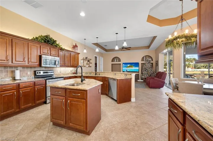 Kitchen featuring pendant lighting, a raised ceiling, sink, an island with sink, and appliances with stainless steel finishes