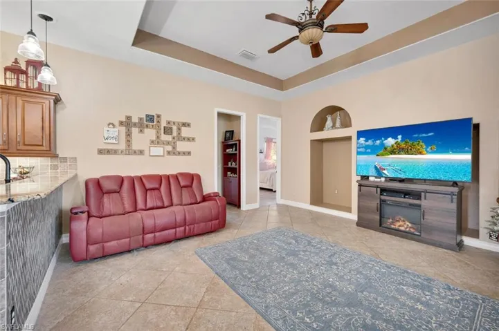 Living room featuring a tray ceiling, ceiling fan, built in features, and light tile patterned flooring