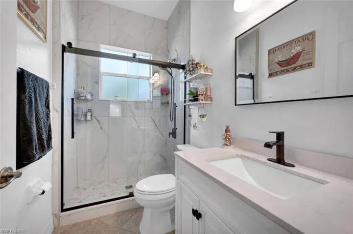 Bathroom with an enclosed shower, vanity, toilet, and plenty of natural light