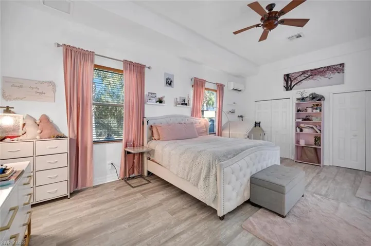 Bedroom featuring a wall mounted air conditioner, light hardwood / wood-style flooring, multiple windows, and ceiling fan