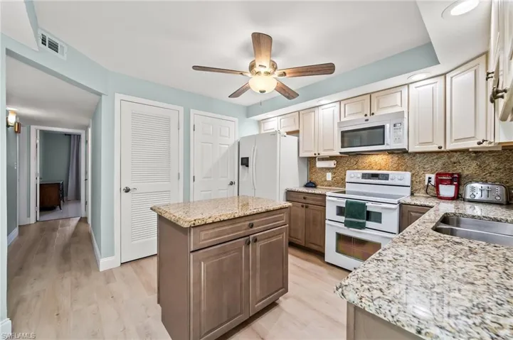 Kitchen with tasteful backsplash, white appliances, light stone countertops, and a kitchen island