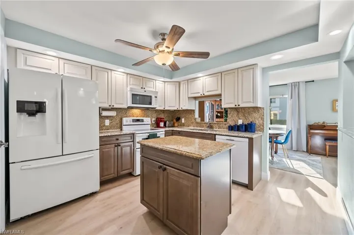 Kitchen featuring white appliances, a kitchen island, ceiling fan, light hardwood / wood-style floors, and backsplash