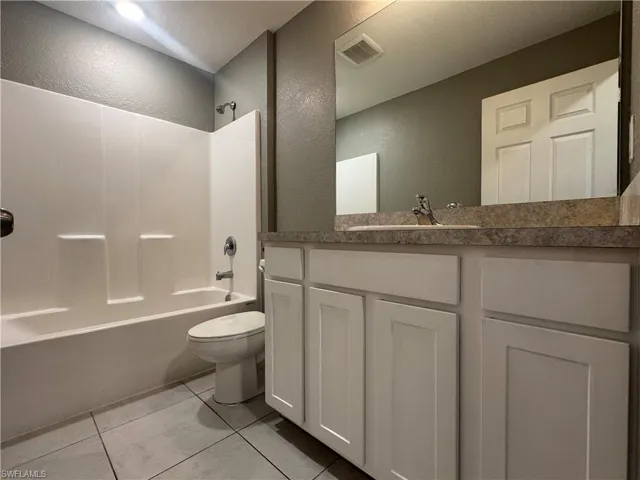Bathroom with vanity, a textured wall, bathtub / shower combination, and light tile patterned flooring