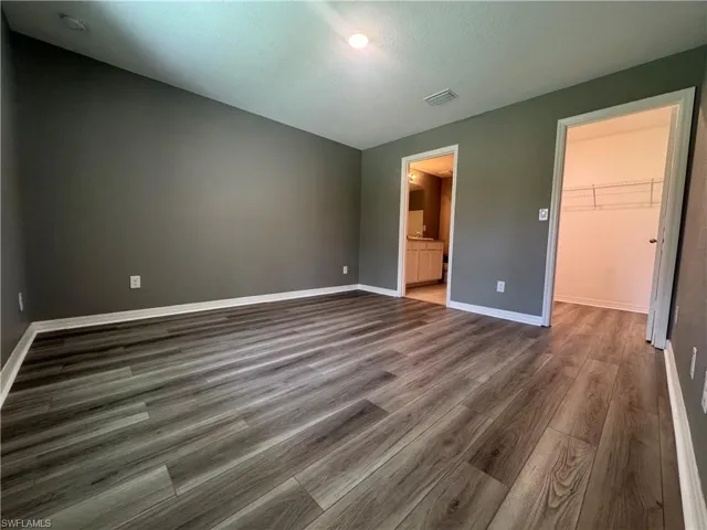 Unfurnished bedroom featuring a walk in closet, dark wood-type flooring, and ensuite bath