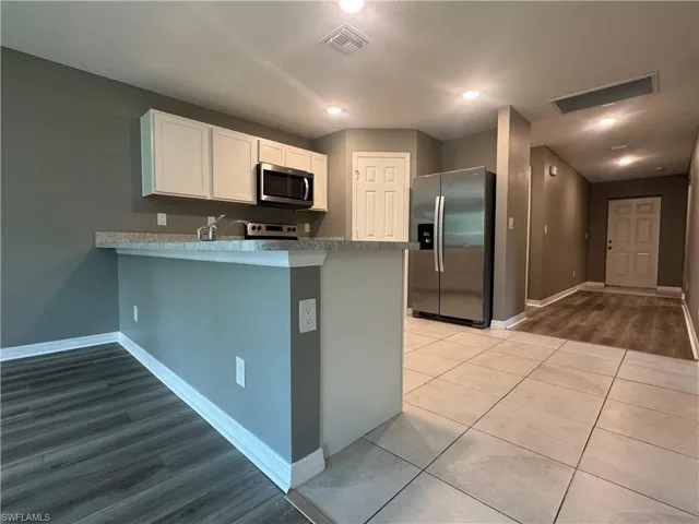 Kitchen with stainless steel appliances, a peninsula, light countertops, white cabinetry, and dark tile patterned flooring