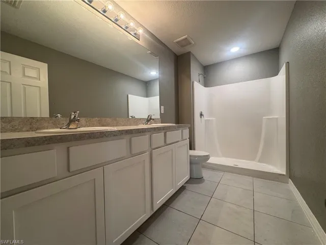 Full bath featuring double vanity, a shower stall, a textured wall, light tile patterned floors, and a textured ceiling