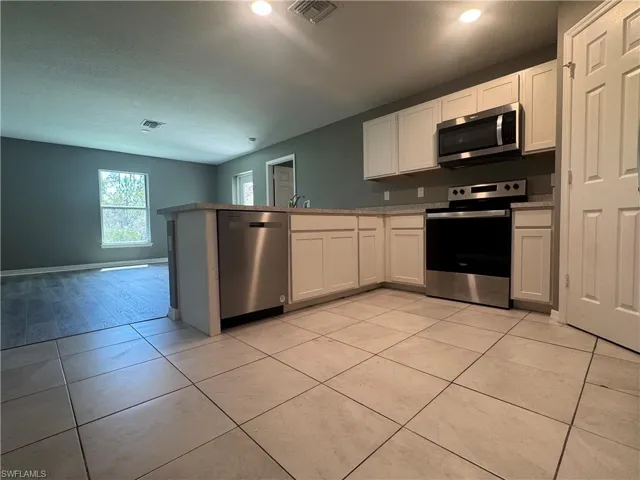 Kitchen featuring stainless steel appliances, white cabinetry, a peninsula, light tile patterned floors, and a textured ceiling