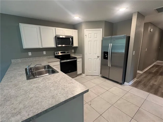 Kitchen with stainless steel appliances, light tile patterned floors, white cabinetry, light countertops, and a peninsula