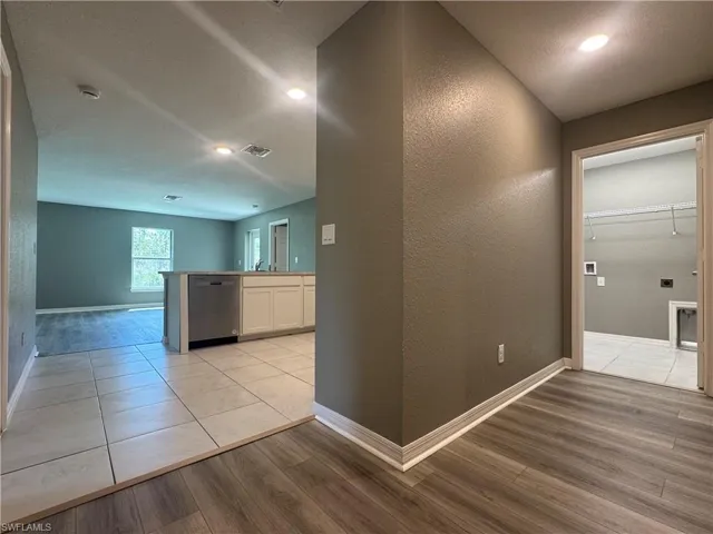 Hall featuring a textured wall, light wood-style floors, and recessed lighting