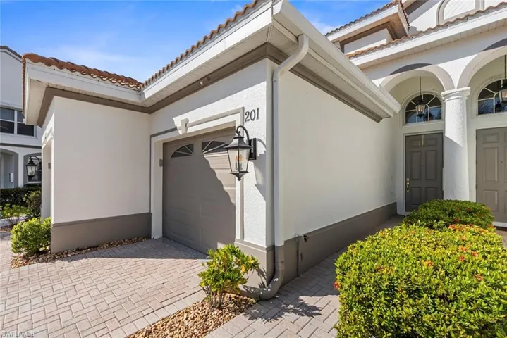 Doorway to property with a garage, a tile roof, stucco siding, and decorative driveway