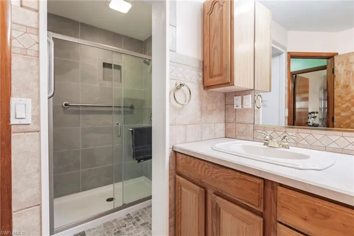 Bathroom featuring tile walls, walk in shower, backsplash, and vanity