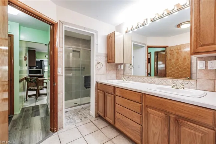 Bathroom featuring backsplash, oversized vanity, dual sinks, hardwood / wood-style flooring, and an enclosed shower
