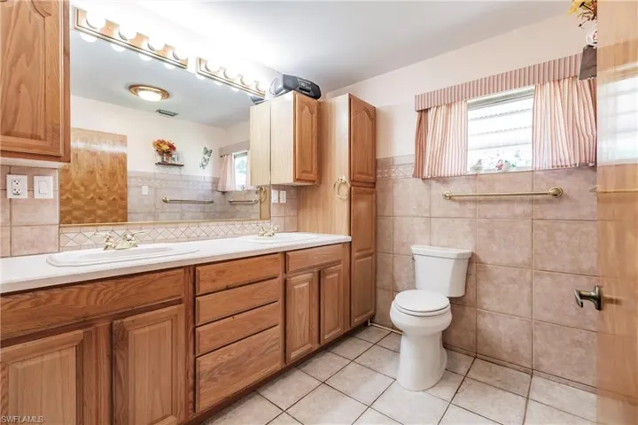 Bathroom featuring tile walls, dual vanity, toilet, tile floors, and tasteful backsplash