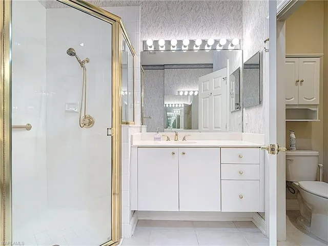 Bathroom with toilet, a stall shower, wallpapered walls, and vanity